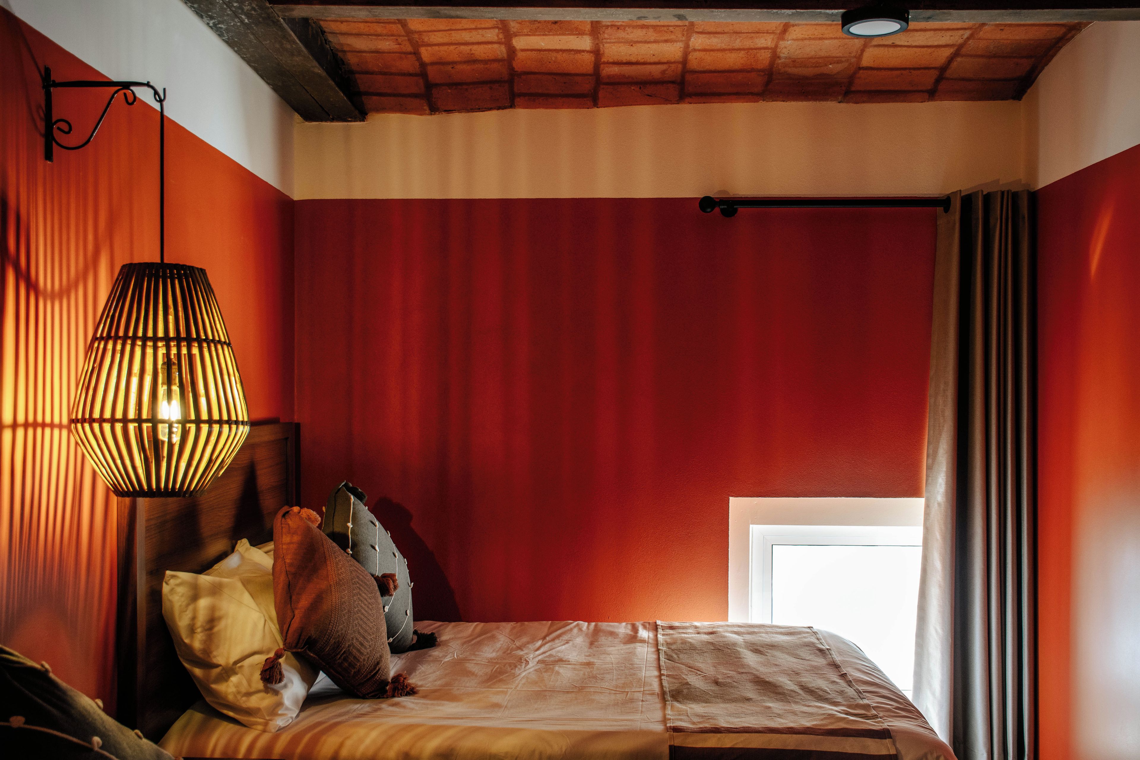 Una habitación con una cama, una lámpara colgante y un ventanal con cortinas.