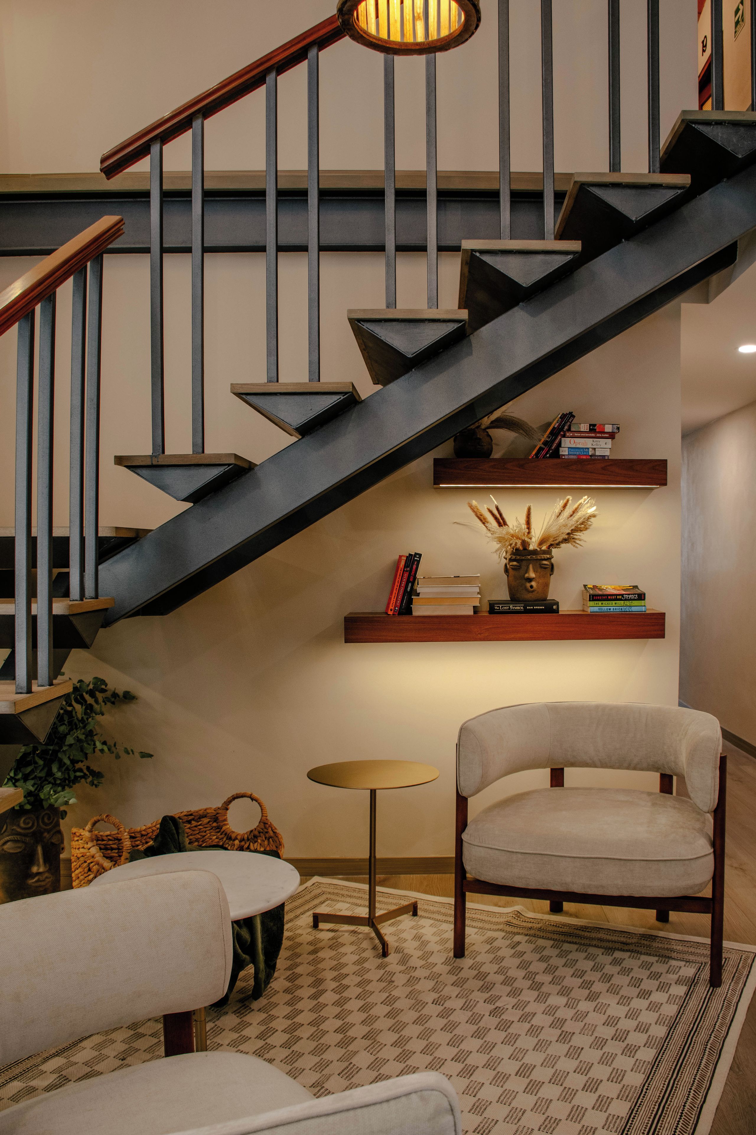 A modern staircase with a dark finish, a wooden handrail, and a wall-mounted shelf with books and decorative items.