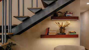 Una moderna scala con finitura scura, ringhiera in legno e una mensola a parete con libri e oggetti decorativi.