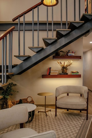 A modern staircase with a dark finish, a wooden handrail, and a wall-mounted shelf with books and decorative items. - Toto Hotel (Mexico City)