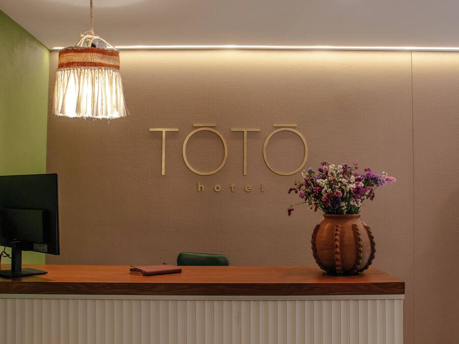 A reception desk with a modern design, a monitor, a vase with flowers, and a wall with the name 'TOTO HOTEL' displayed.
