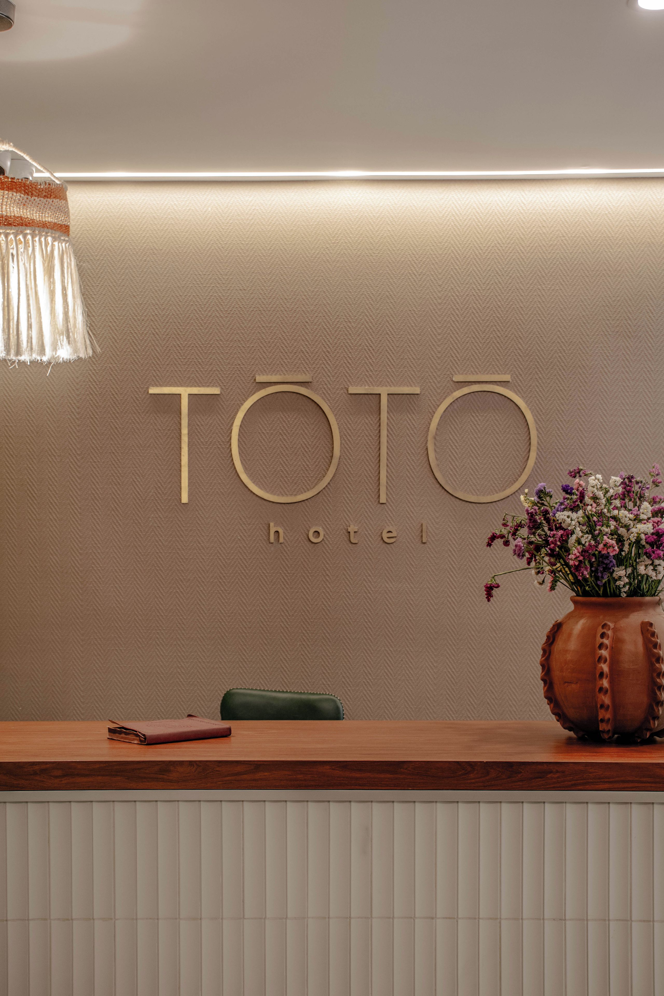 Un mostrador de recepción con un letrero que dice 'TOTO hotel' y un florero con flores.