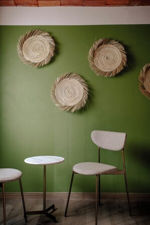 A room with a green wall, a round woven wall hanging, a round table, and a chair.