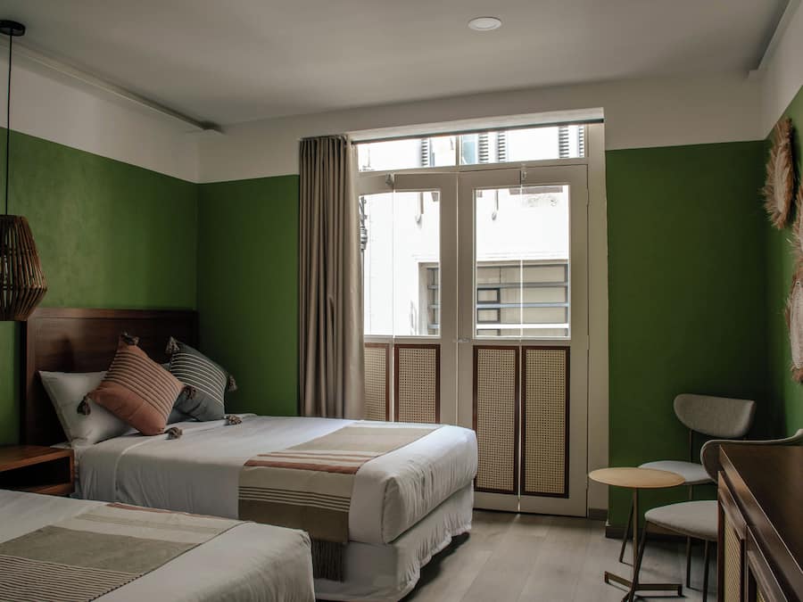 A hotel room with a bed, a desk, and a chair. There is a window with curtains.