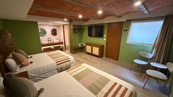 Una habitación con dos camas, una kitchenette pequeña, un ventanal con cortinas y una zona de estar con sillas.
