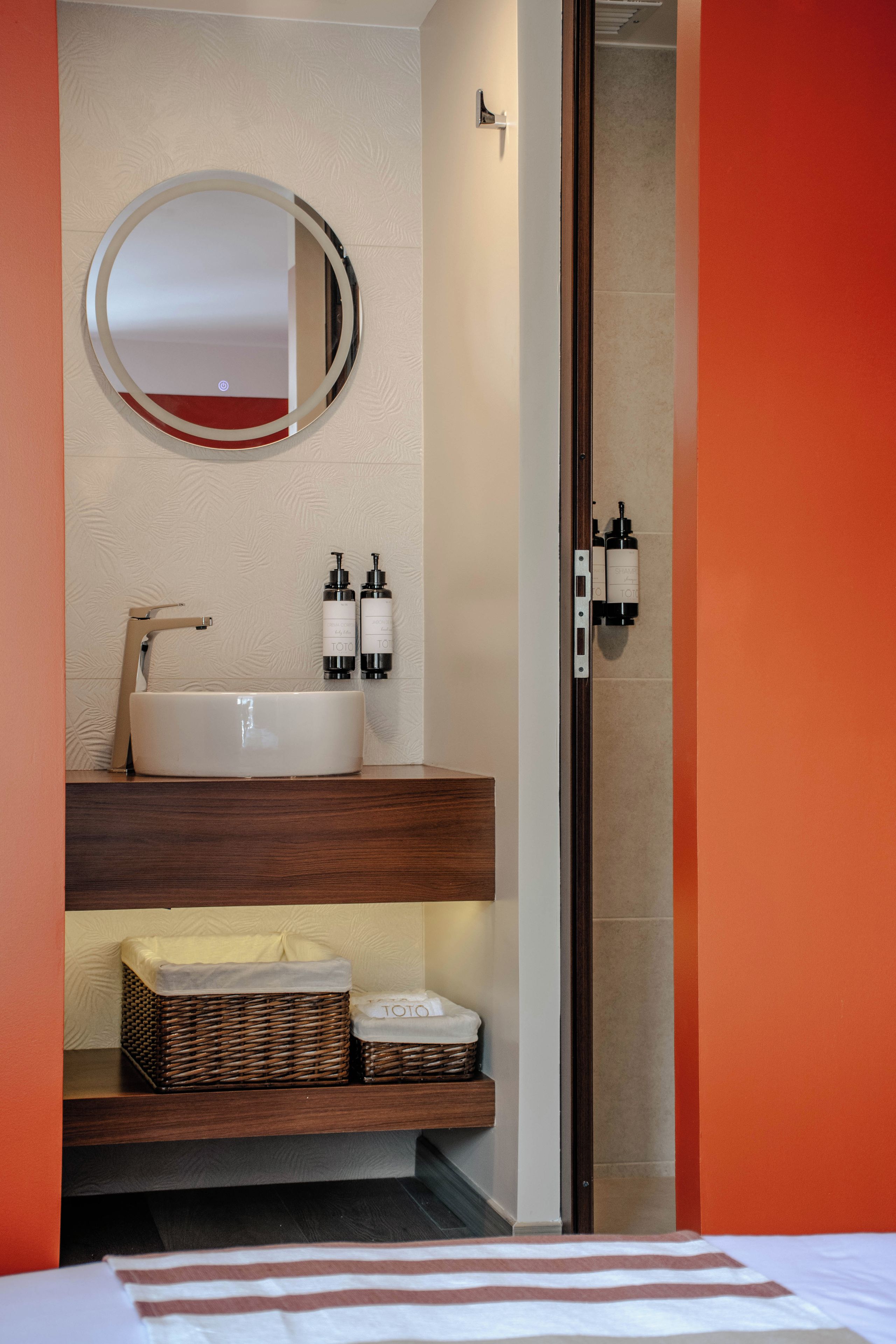 A bathroom with a white sink, two bottles of shampoo, a mirror, and a wooden shelf with a basket.