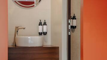 A bathroom with a white sink, two bottles of shampoo, a mirror, and a wooden shelf with a basket.