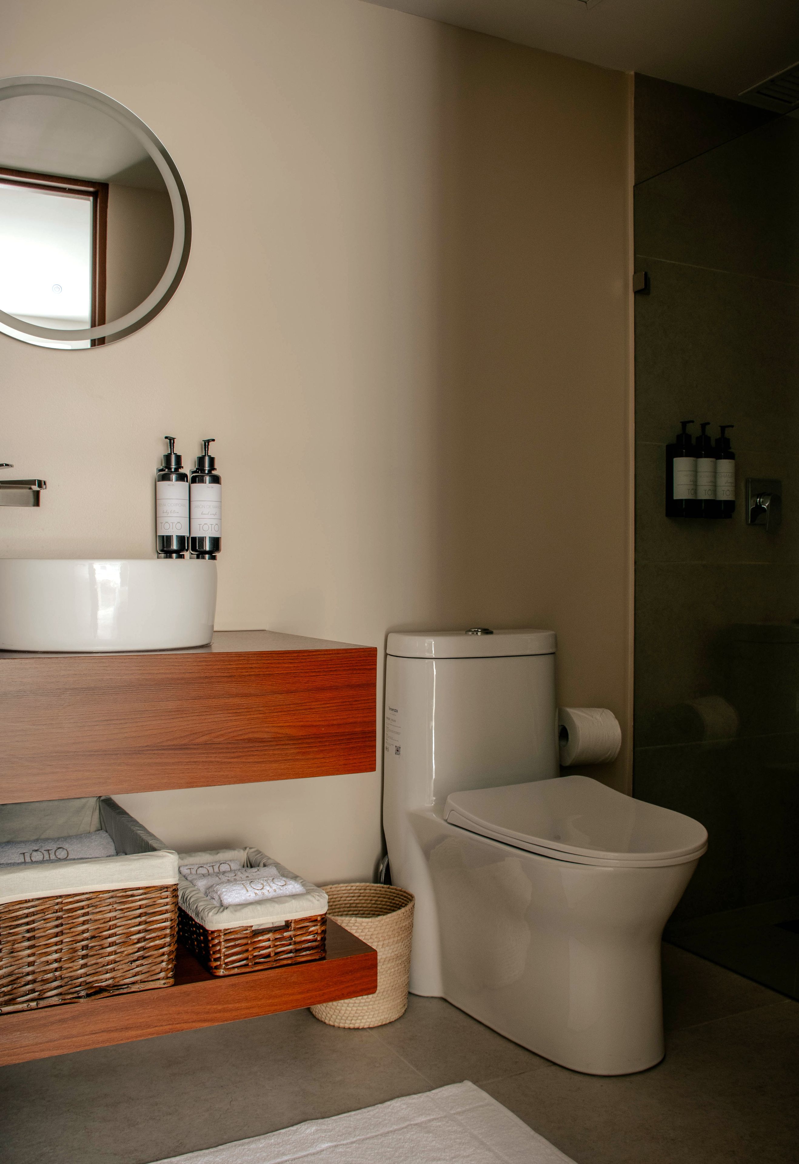 Un bagno moderno con un WC, un lavandino e uno specchio. Sono presenti articoli da toilette sul lavandino e un cesto a pavimento.