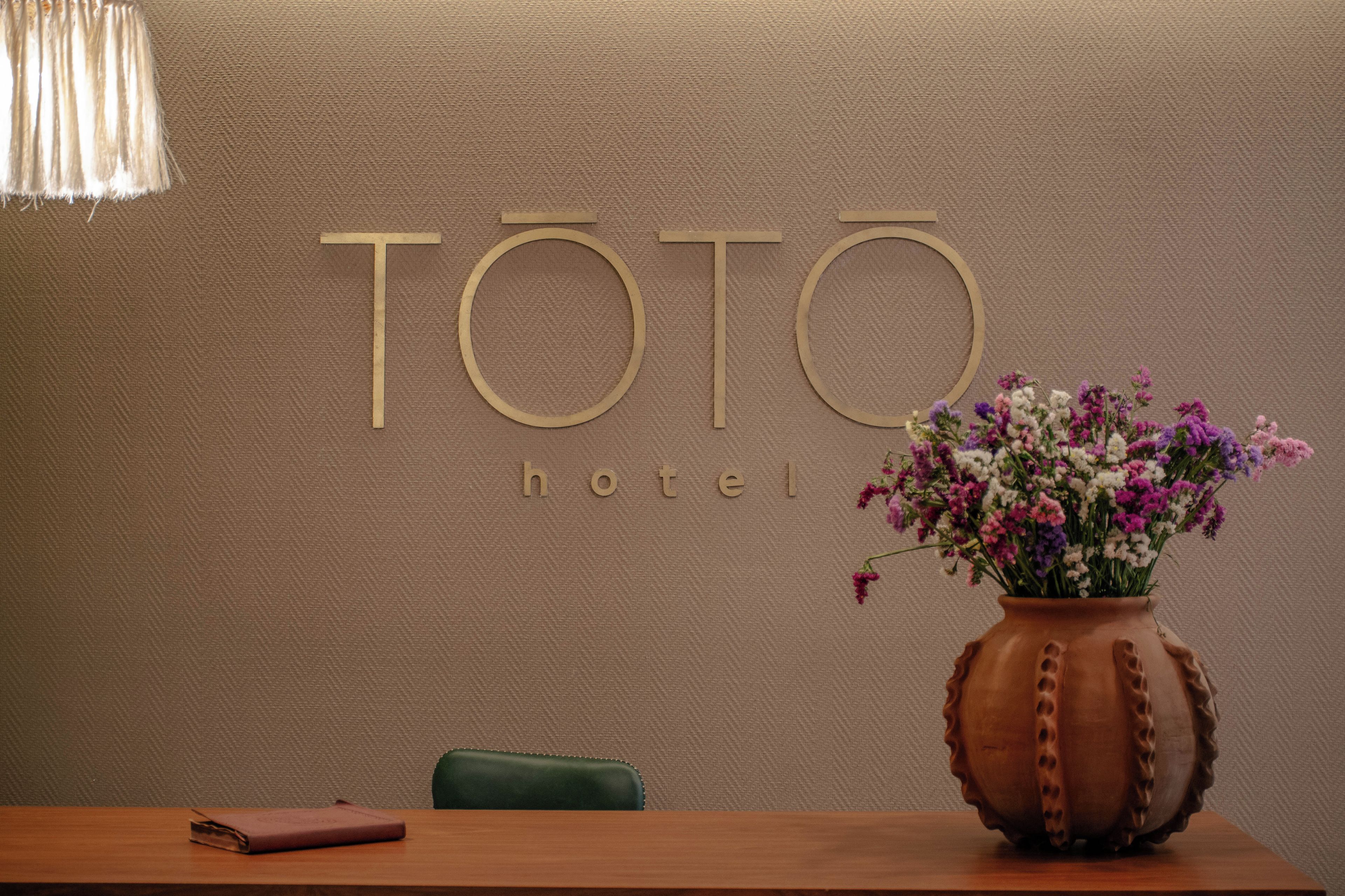 A reception desk with a wooden table, a green chair, a vase with flowers, and a sign that reads 'TOTO hotel'.