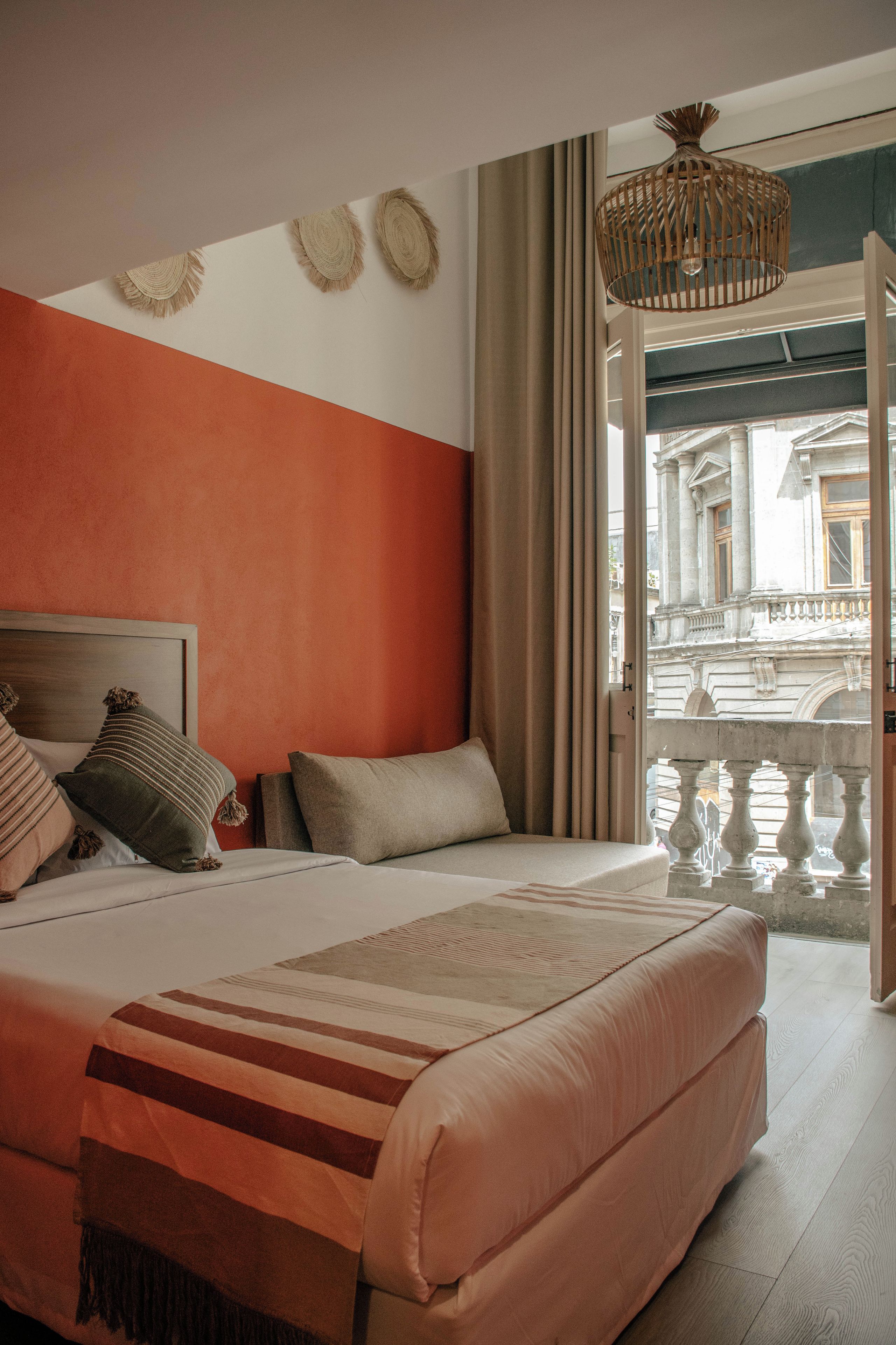 A bedroom with a bed, pillows, a headboard, a window with curtains, and a view of a building outside.