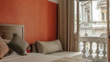 Una camera da letto con un letto, cuscini, una testiera, una finestra con tende e vista su un edificio.