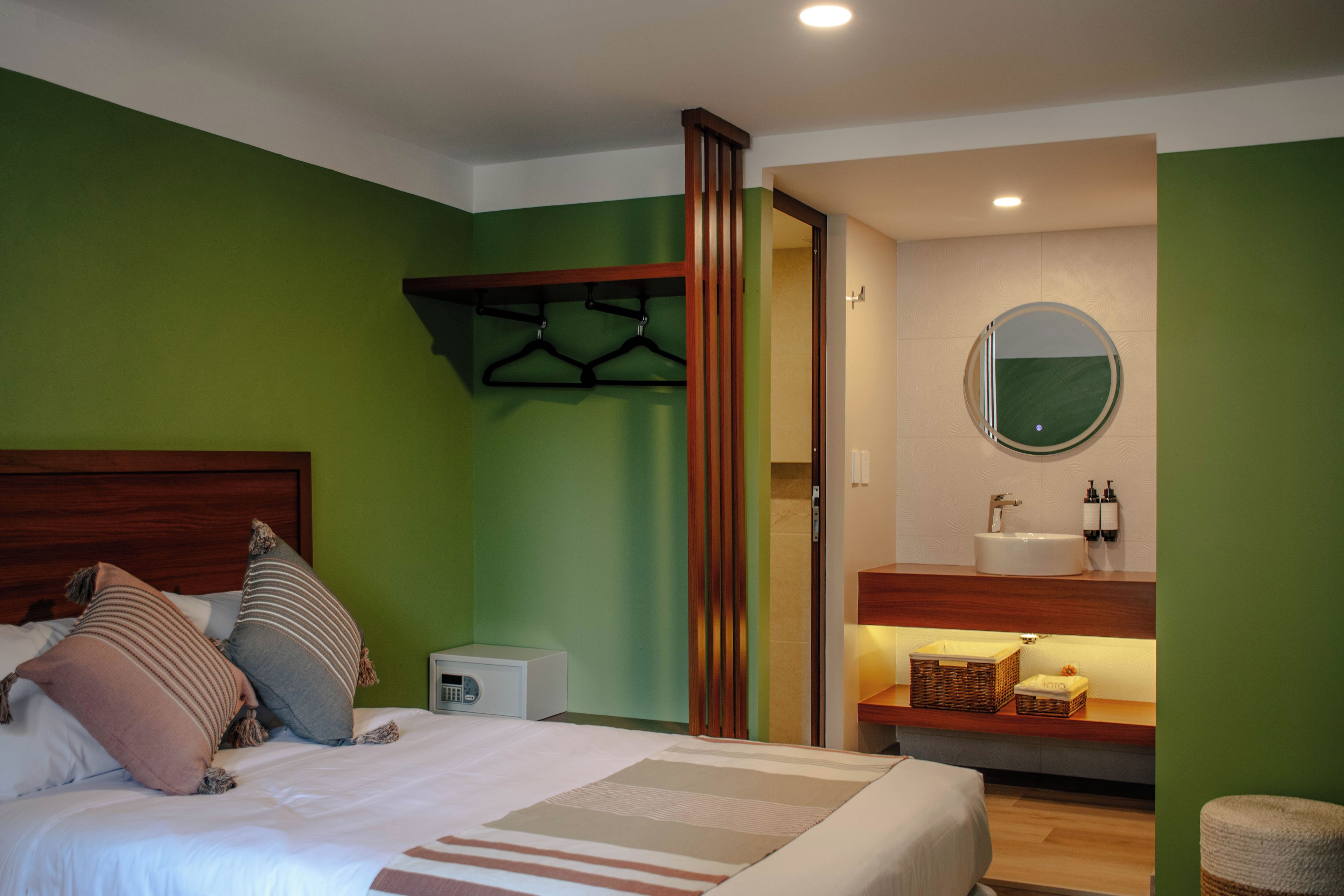 A hotel room with a bed, a bedside table, a mirror, and a bathroom visible through an open door.