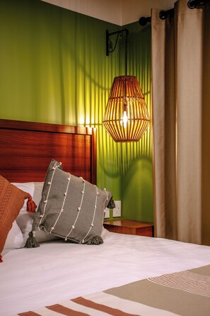 A hotel room with a bed, pillows, a wooden headboard, a green wall, a hanging lamp, and a curtain. - Toto Hotel (Mexico City)