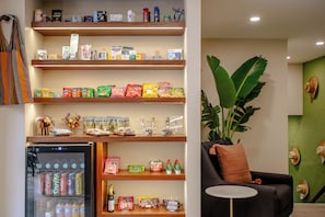 A well-organized shelf with snacks, a refrigerator stocked with beverages, and a cozy seating area with a plant. - Toto Hotel (Mexico City)