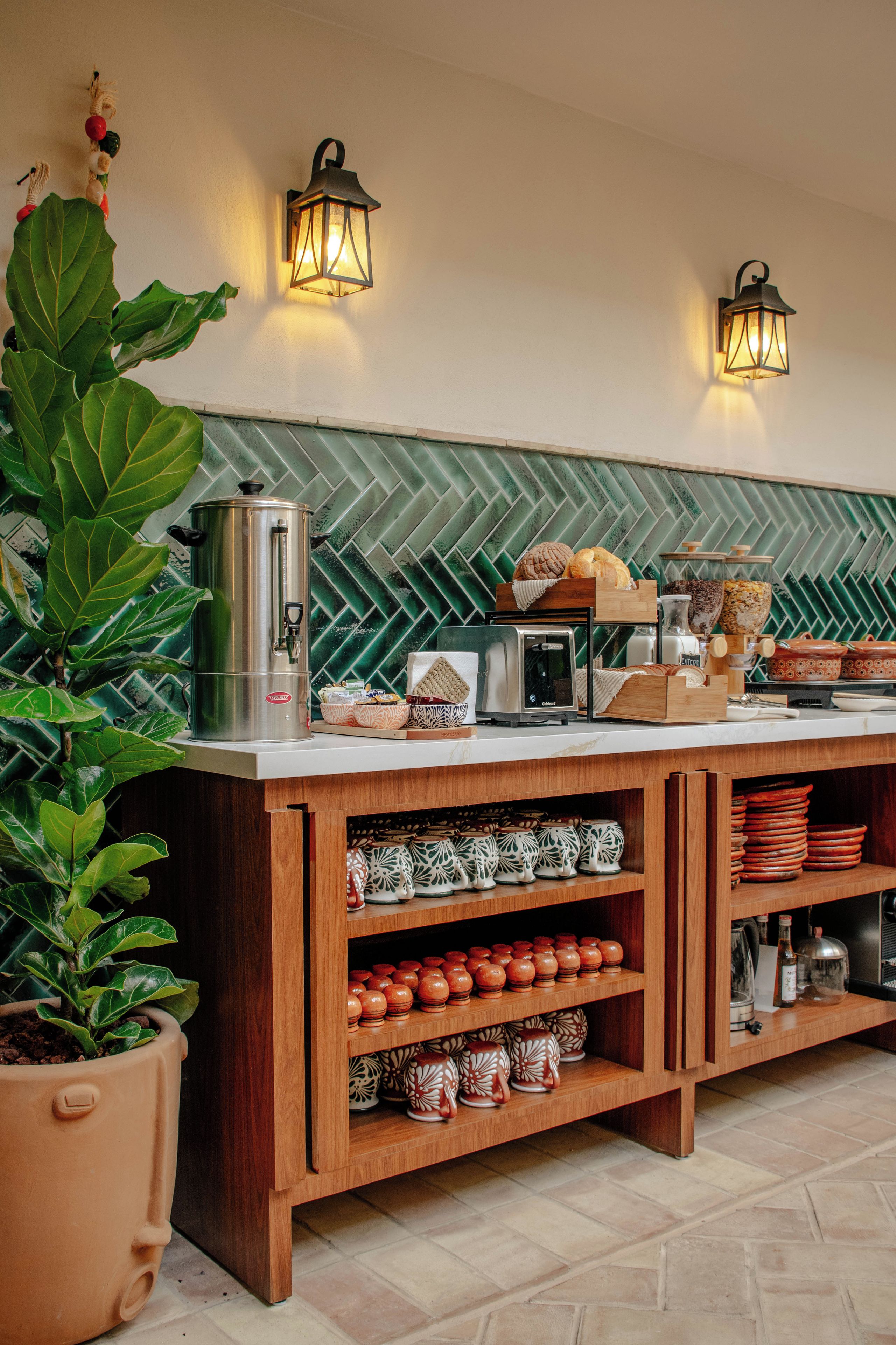 A breakfast bar with a herringbone tile backsplash, a coffee machine, and shelves with ceramic mugs and plates.