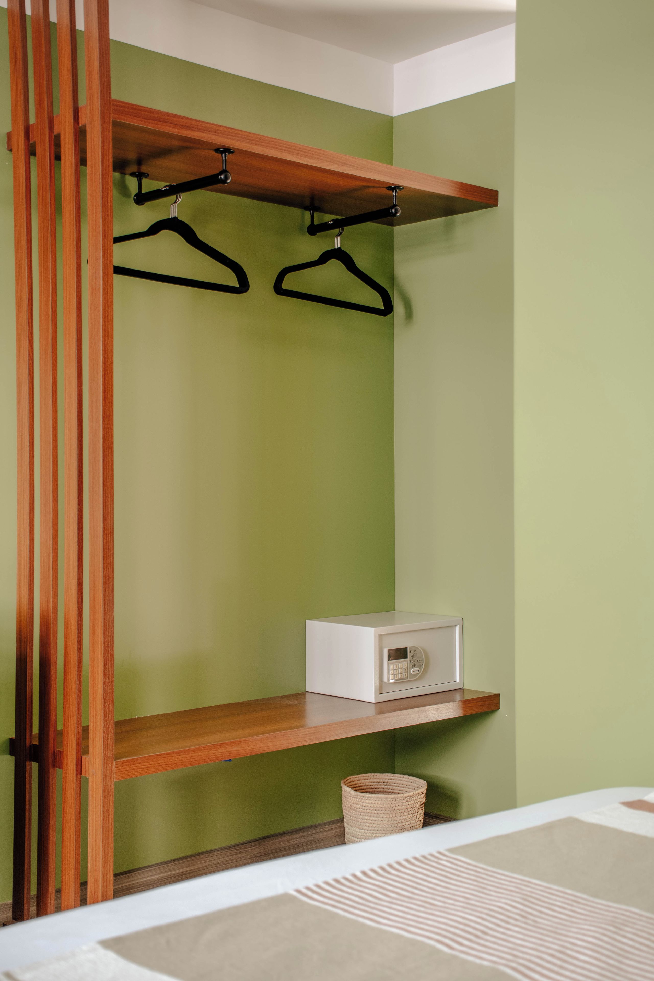 A room with a green wall, a wooden shelf with a radio, and a hanging clothes rack.