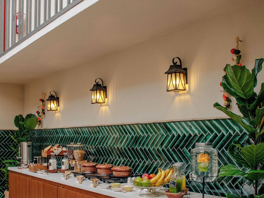 A buffet setup with a long wooden counter, wall-mounted lights, and a green patterned backsplash.