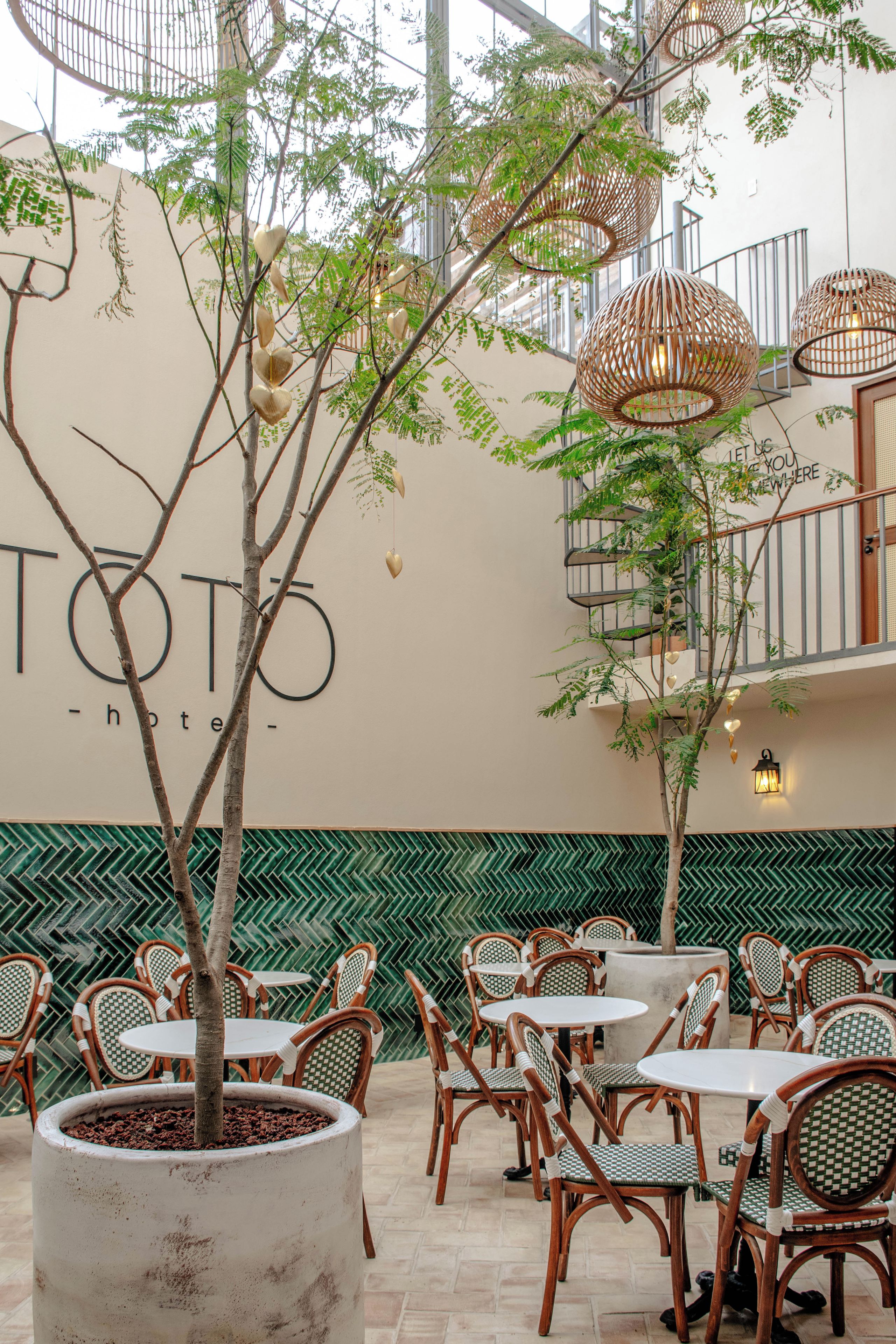 An outdoor seating area with wicker chairs and tables, surrounded by greenery and a wall with the text 'TOTO hotel'.