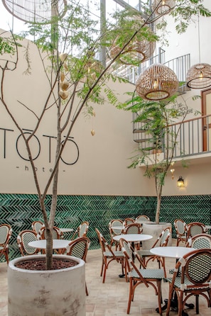 An outdoor seating area with wicker chairs and tables, surrounded by greenery and a wall with the text 'TOTO hotel'.