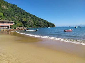A beach with boats, a building, and a forested hillside. - Beach house in Picinguaba, Beach house, House in Ubatuba, House in Picinguaba. (Ubatuba)