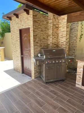 An outdoor barbecue grill with a stone wall backdrop, a wooden door, and a tiled patio. - Luxurious Colonial Mansion in Puerto Plata With Private Pool (Puerto Plata)