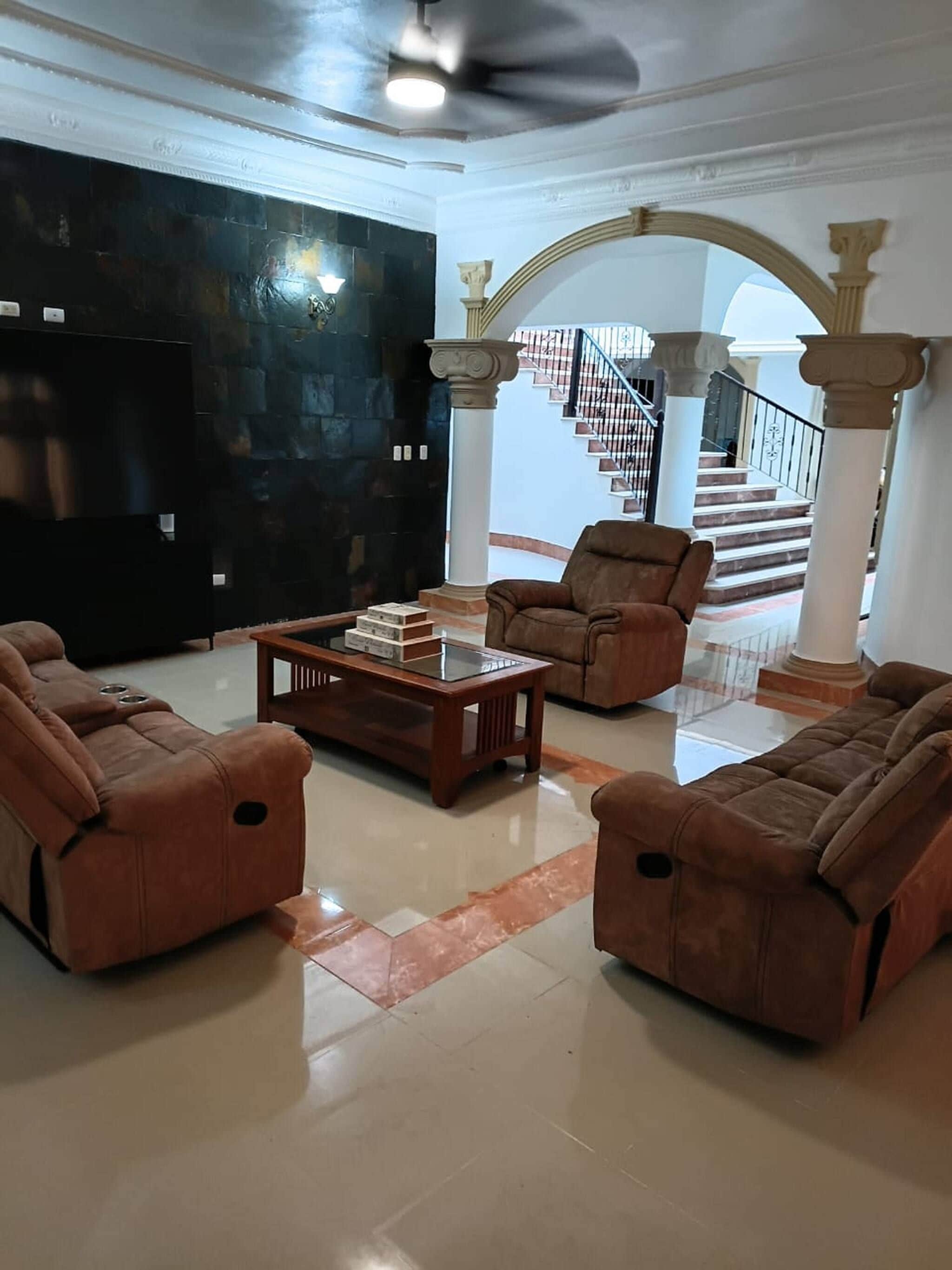 A spacious living room with a modern design, featuring a large black wall, a glass coffee table, and two brown leather sofas.