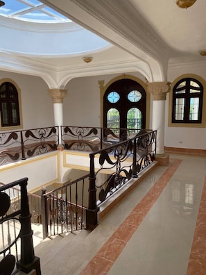 A spacious interior with a high ceiling, a balcony with ornate railing, and large windows allowing natural light. - Luxurious Colonial Mansion in Puerto Plata With Private Pool (Puerto Plata)