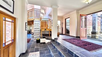 Un interior espacioso con una escalera que conduce a un balcón de madera, suelo de piedra y vistas al exterior.
