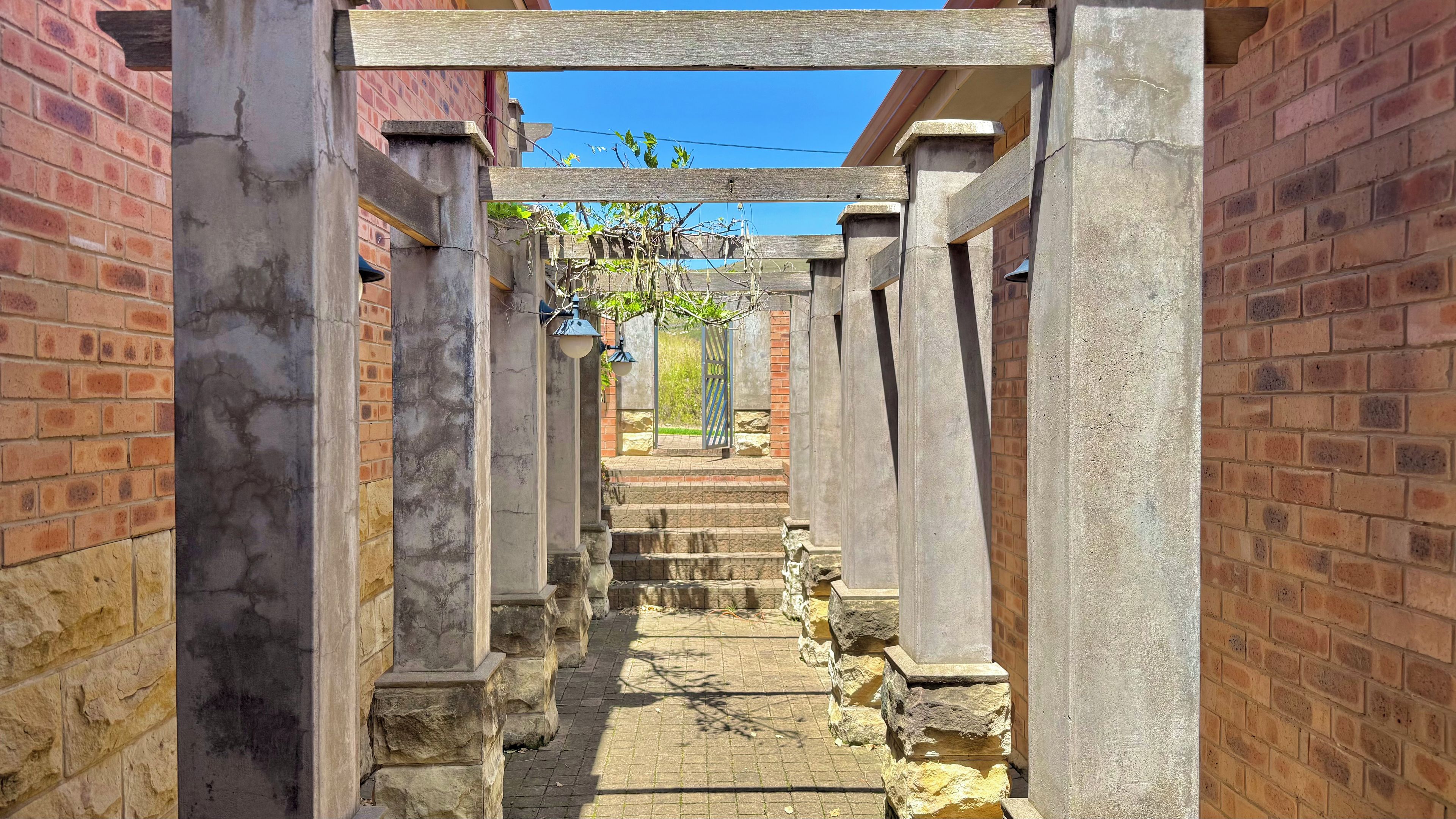A stone pathway leading to a gated entrance with a wooden pergola overhead.