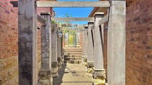 A stone pathway leading to a gated entrance with a wooden pergola overhead. - The Eyrie Guesthouse (Clarens)