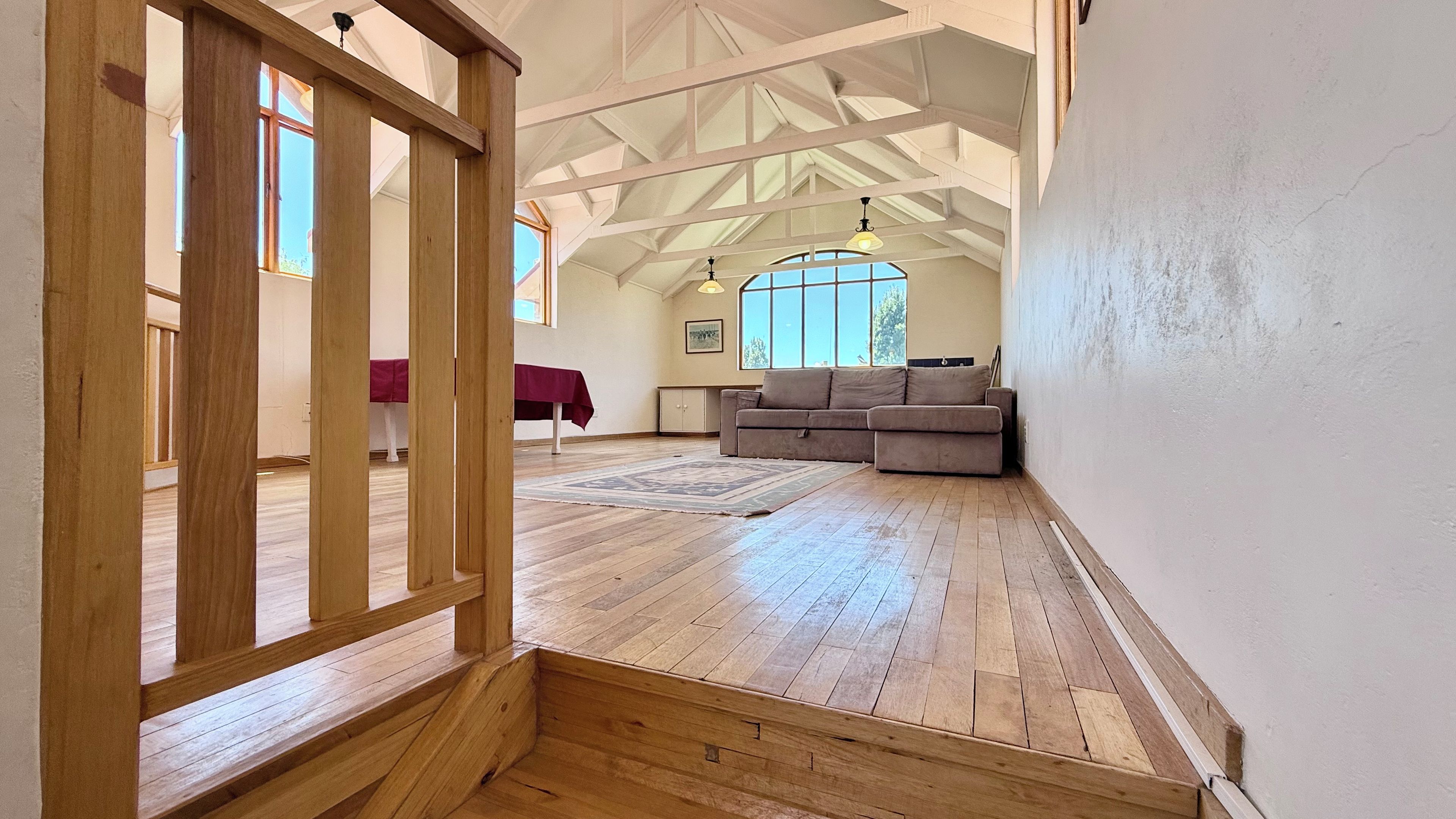 A spacious room with wooden flooring, a sofa, and a dining table with a red tablecloth.