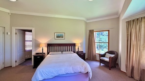 Una habitación de hotel con una cama grande, dos mesitas de noche con lámparas, una silla, una ventana con cortinas y un cuadro en la pared.
