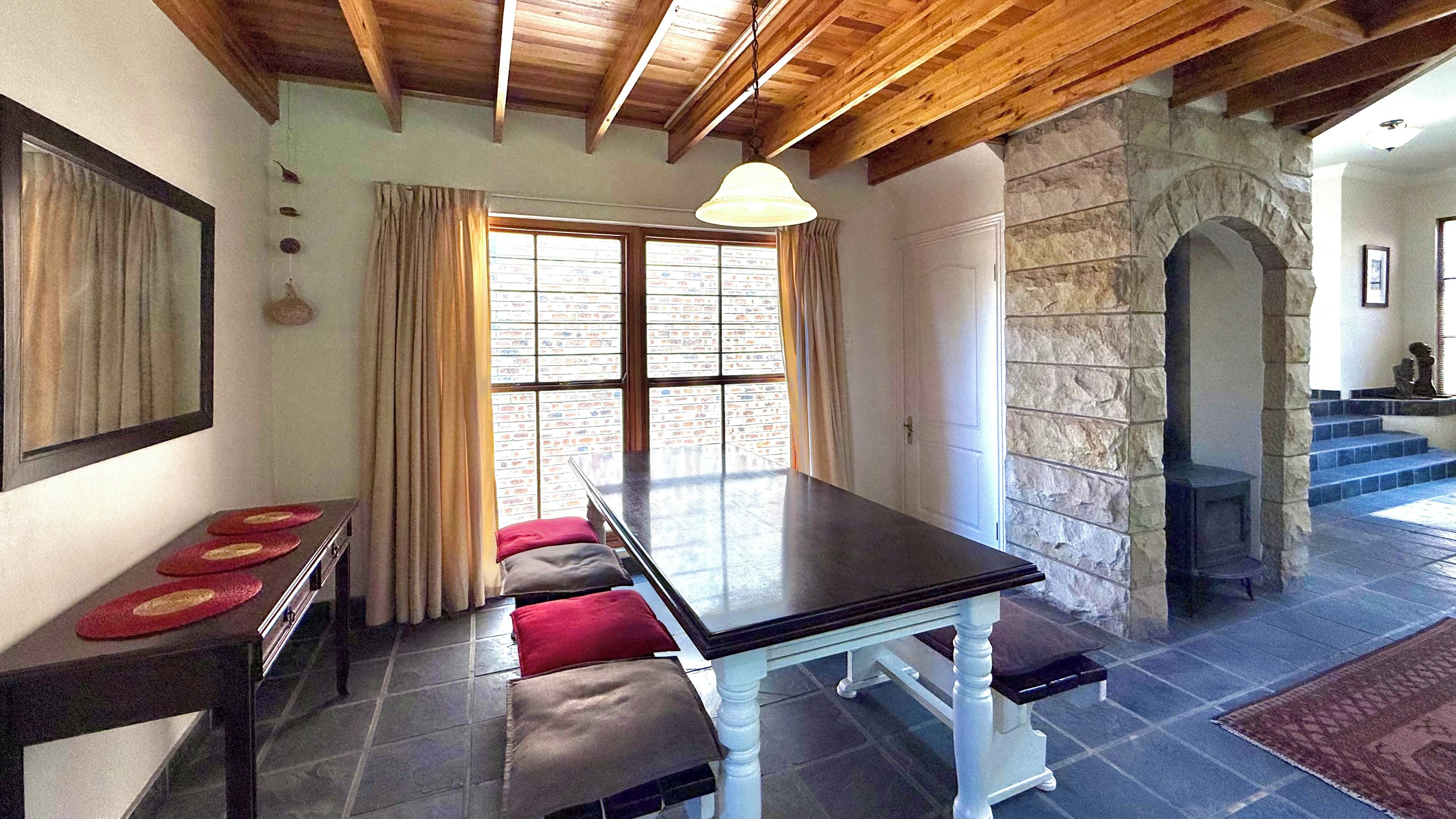 A dining area with a table and benches, a stone wall, and a staircase leading to an upper level.