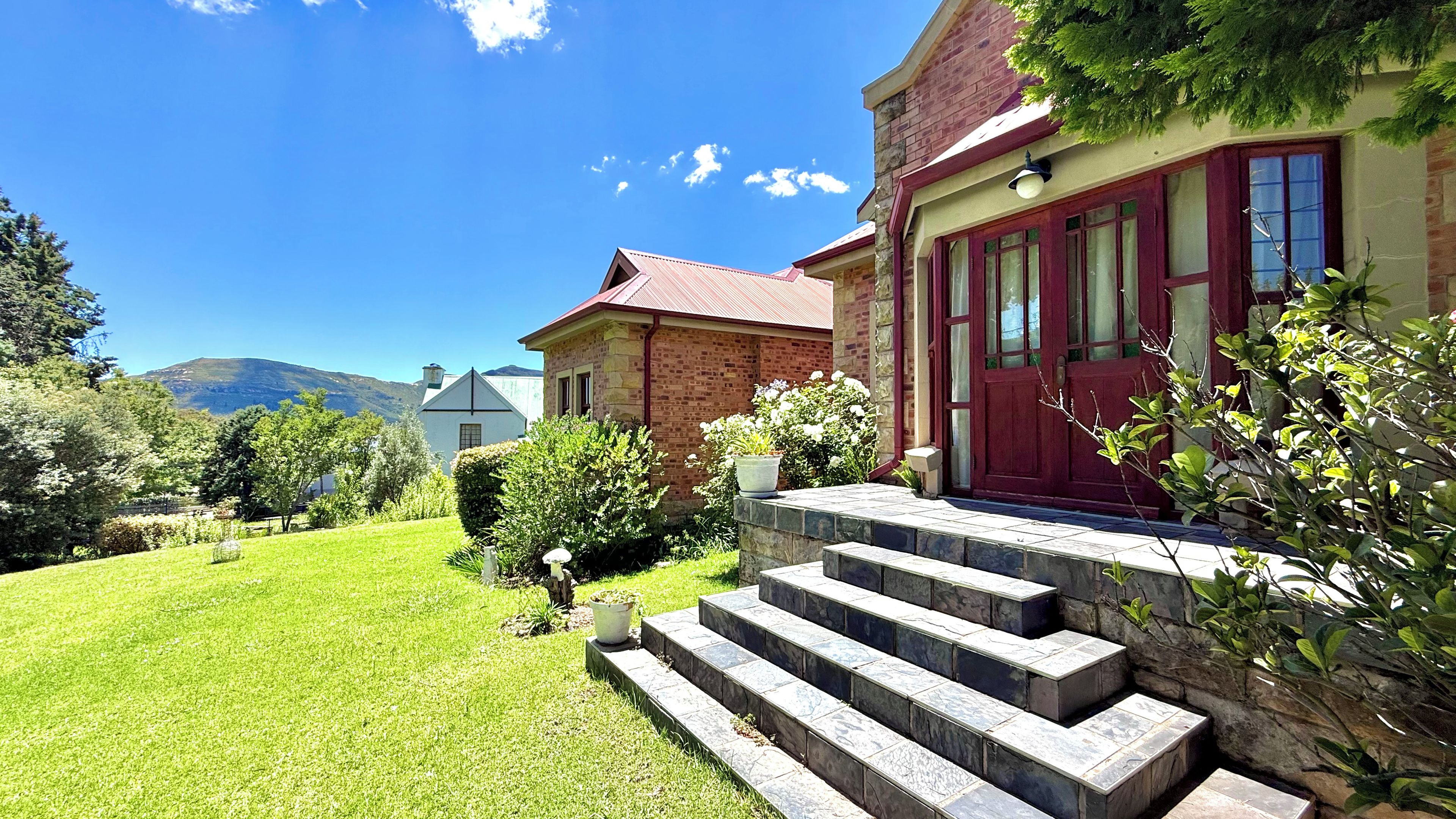 A two-story house with a red door, stone steps, and a well-maintained lawn.