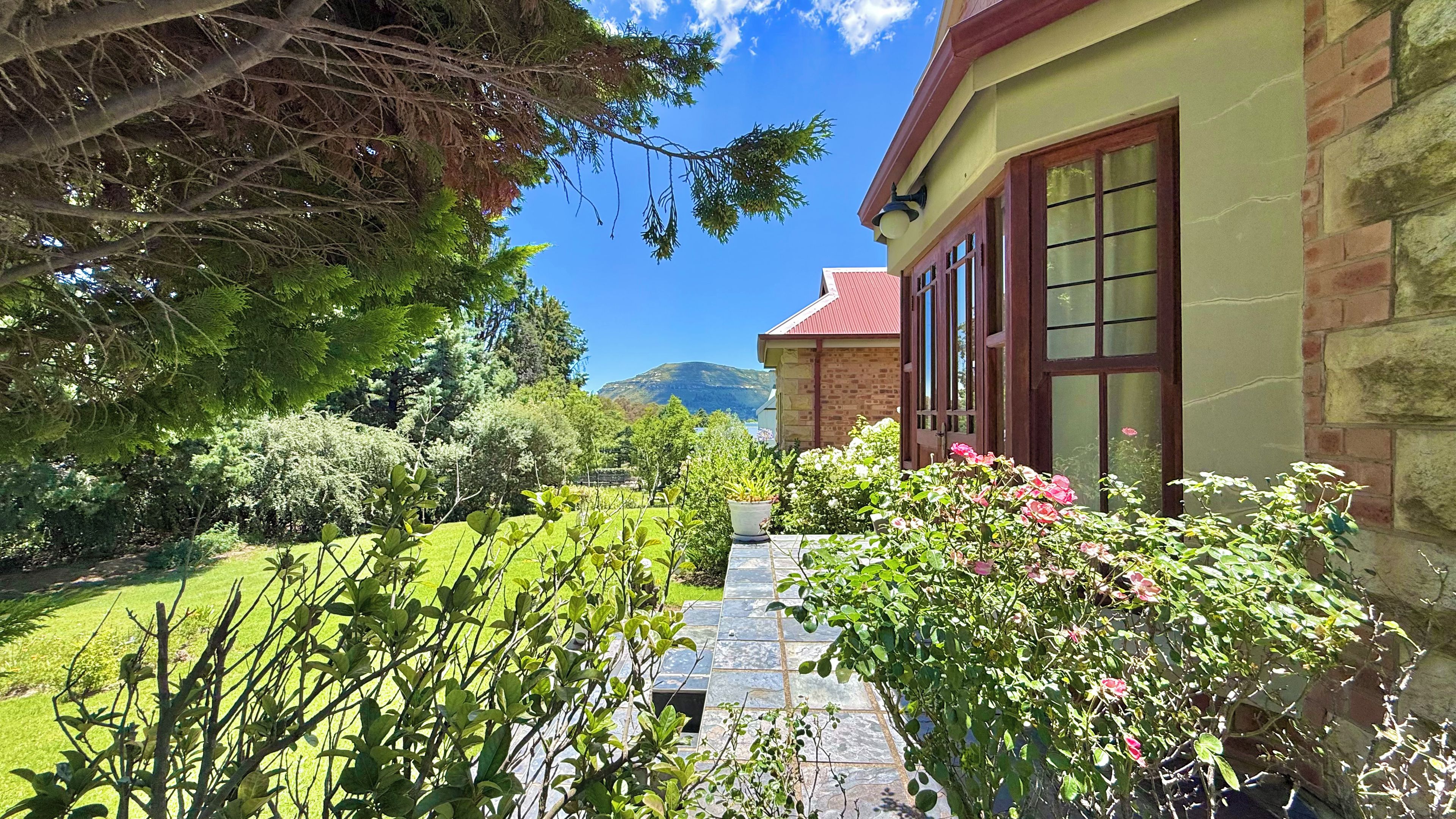 A stone building with a red roof, a paved pathway, and lush greenery.