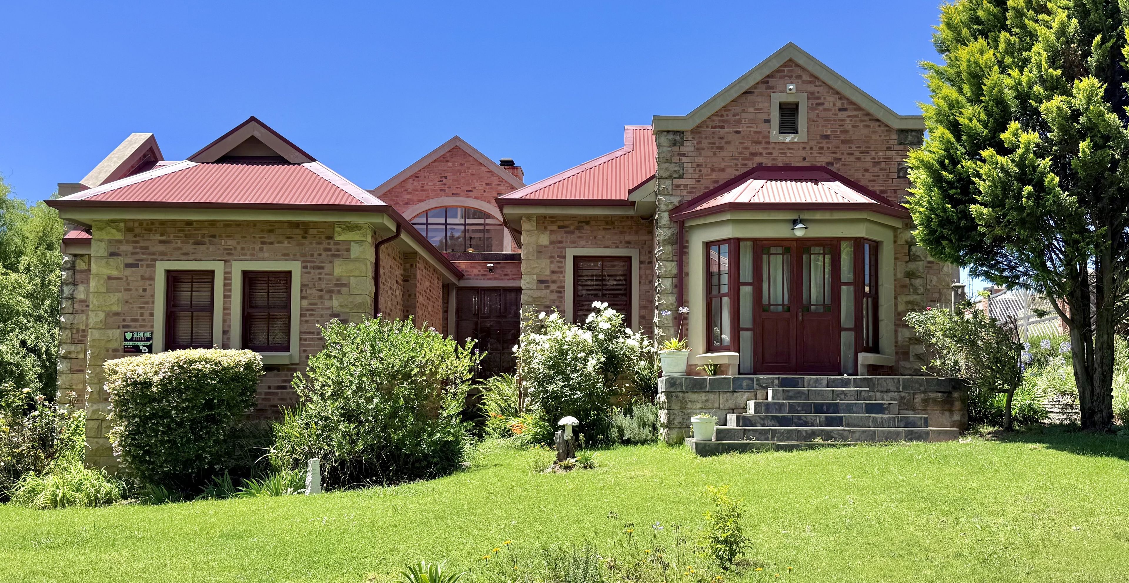 A two-story stone house with a red roof, a front porch, and a well-maintained garden.