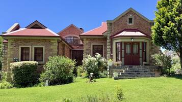 A two-story stone house with a red roof, a front porch, and a well-maintained garden.