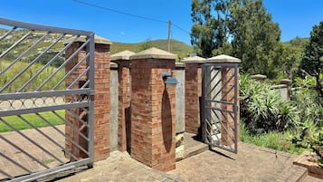 Una entrada protegida con un portón metálico y pilares de ladrillo, rodeada de vegetación y un paisaje montañoso.