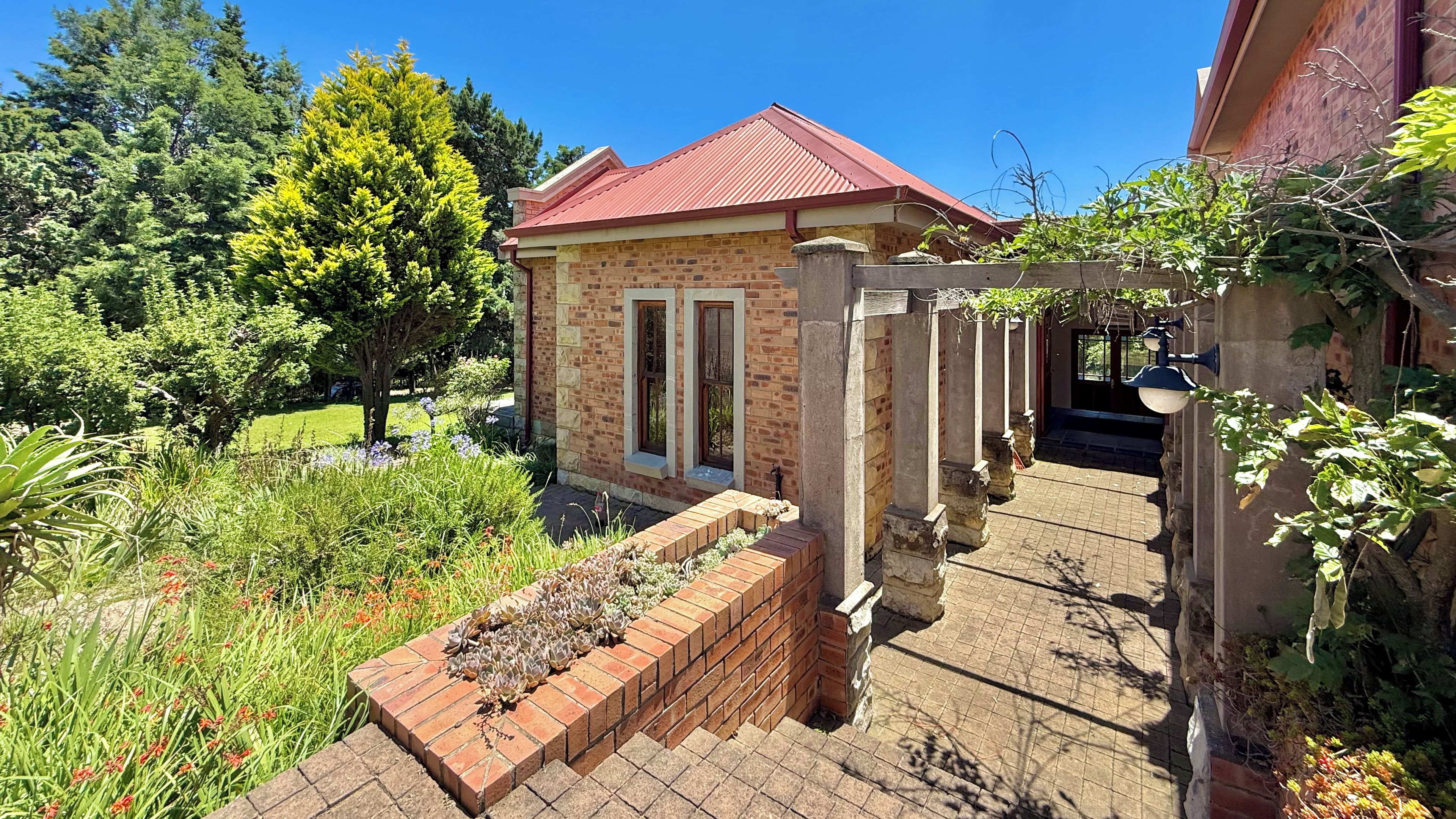 A small brick building with a red roof, surrounded by a garden with various plants and flowers.