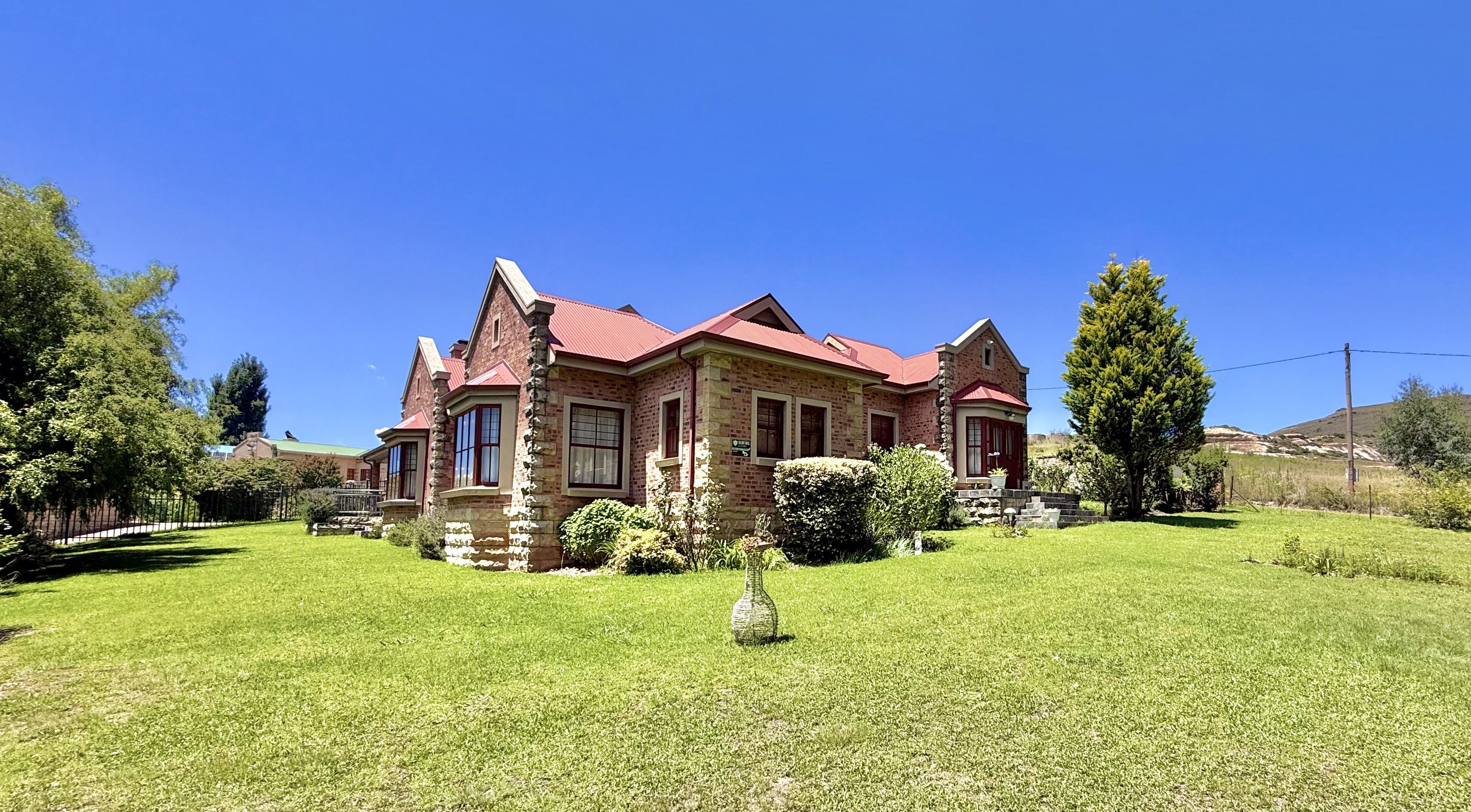 A two-story stone house with a red roof, surrounded by a well-maintained lawn and trees.
