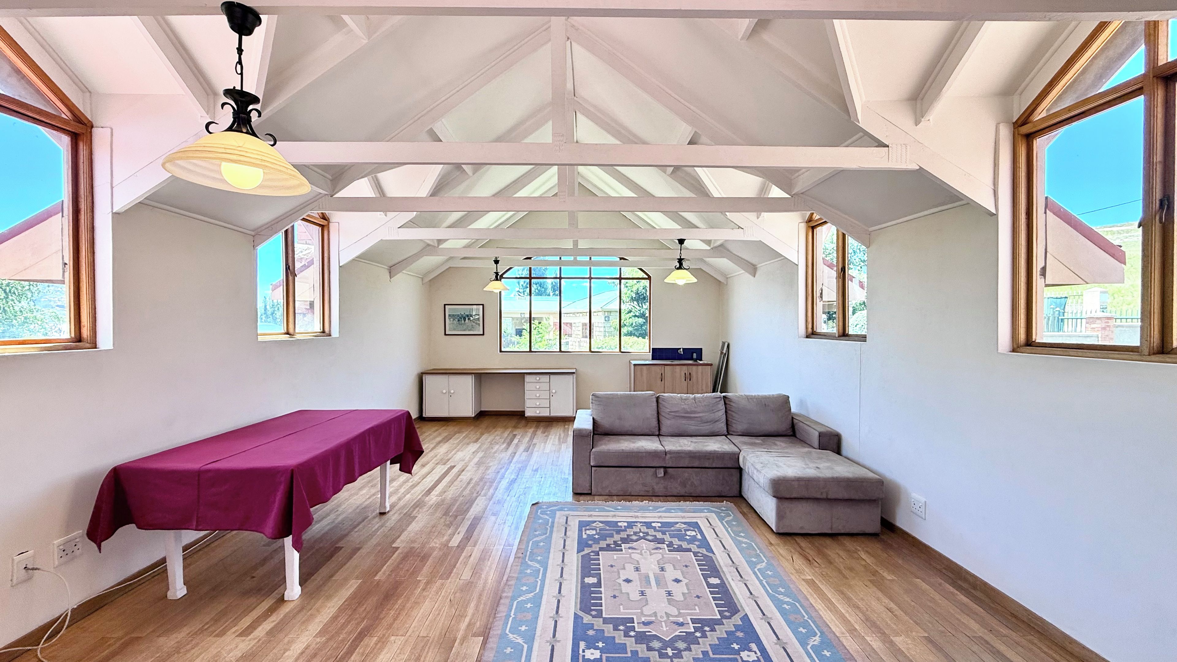 A spacious room with a high ceiling, a dining table, a sofa, and a patterned rug.