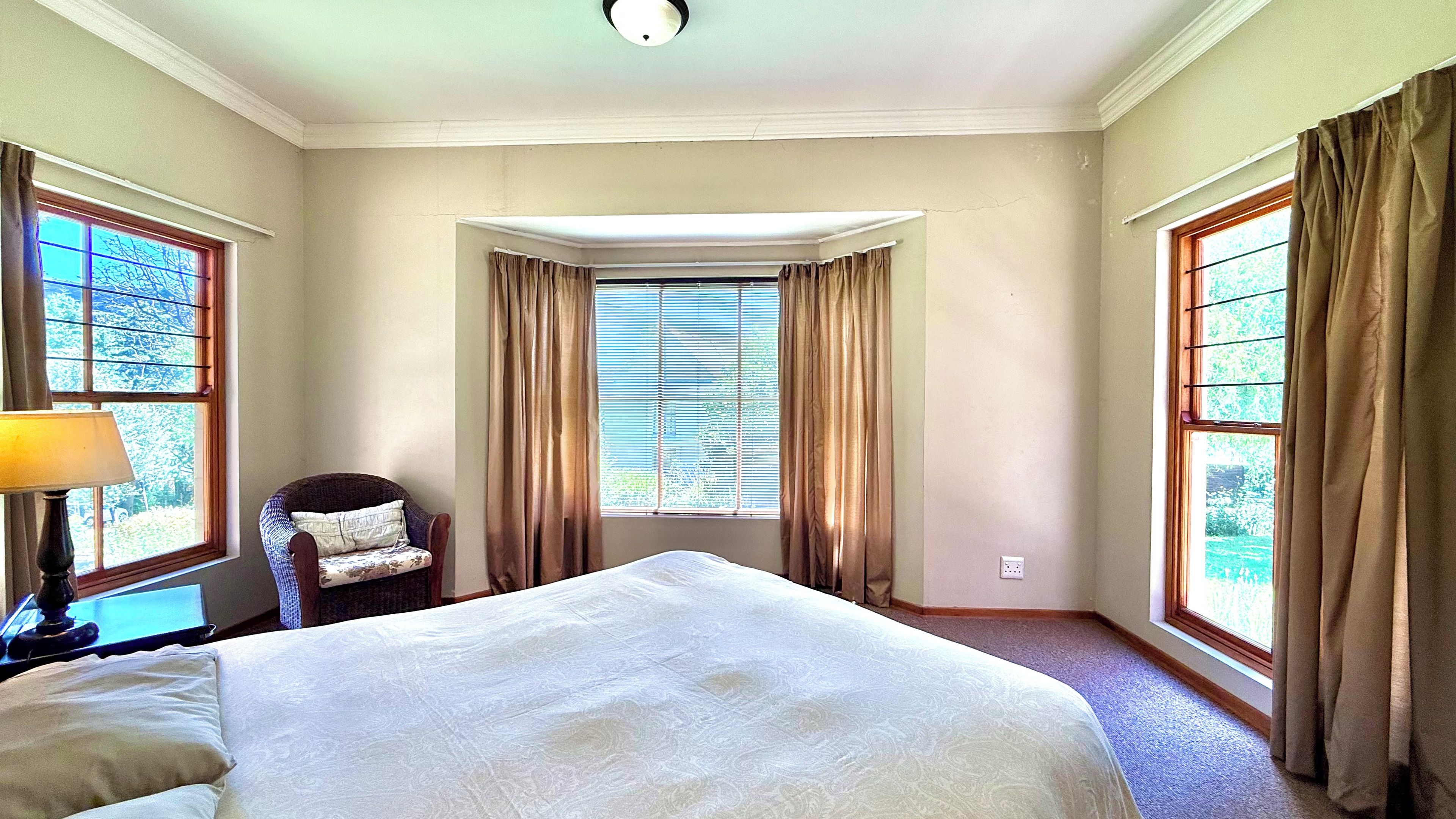 A hotel room with a large bed, a chair, a desk with a lamp, and a window with curtains.