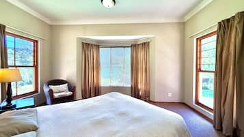 A hotel room with a large bed, a chair, a desk with a lamp, and a window with curtains.
