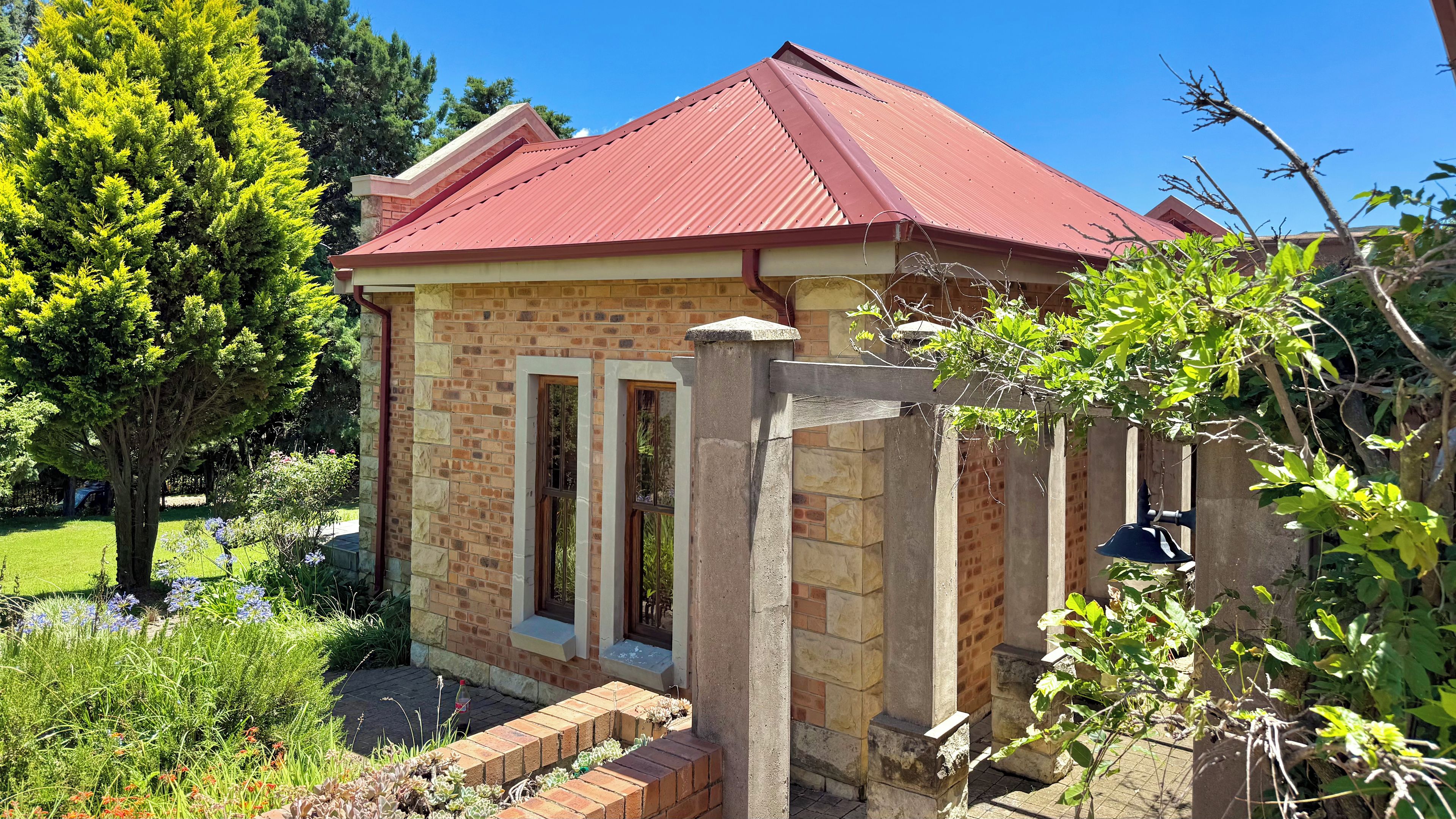 A brick building with a red roof, a stone entrance, and a garden with various plants.