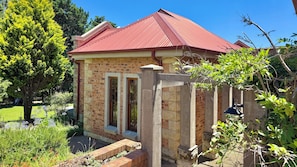 A brick building with a red roof, a stone entrance, and a garden with various plants. - The Eyrie Guesthouse (Clarens)