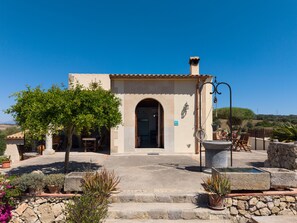 A building with a tiled roof, a stone entrance, and a small garden with potted plants. - Es Turo Des Bessons by Rentallorca (Petra)