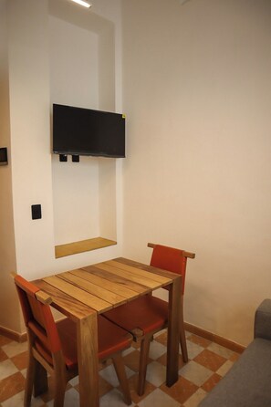 A dining area with a wooden table and chairs, a mounted flat-screen TV, and a checkered floor. - Gran Suite Loft Guadalajara Centro SF (Guadalajara)