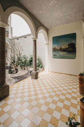 A spacious courtyard with a checkered floor, columns, and a painting of a cityscape on the wall. - Gran Suite Loft Guadalajara Centro SF (Guadalajara)