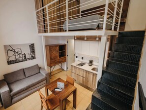 A compact living space with a loft bed, kitchenette, dining area, and a staircase. - Loft en el Centro Histórico de GDL (Guadalajara)