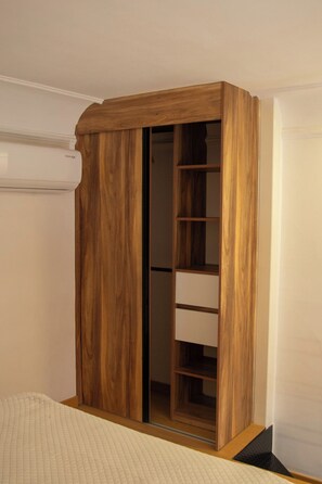 Ein Schlafzimmer mit einem Holfischschrank, einem Bett mit gesteppter Bettdecke und einer weißen Wand.